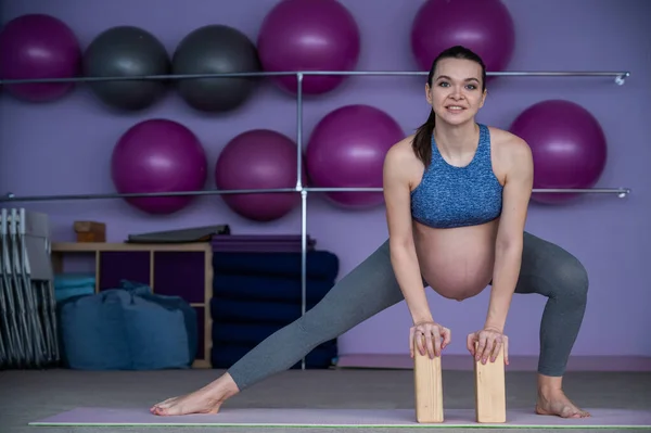 En gravid europeisk kvinna gör pilates ensam. Den förväntansfulla mamman under den sista trimestern tränar yoga med hjälp av yogablock. — Stockfoto