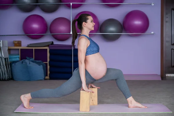 Вагітна гнучка європейська жінка займається фітнесом. Майбутня мати в останньому триместрі вагітності практикує йогу за допомогою блоків йоги.. — стокове фото