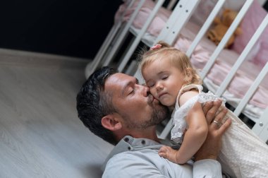 Kafkasyalı adam sırt üstü uzanıyor ve kızını çocuk odasında onun üstünde tutuyor.