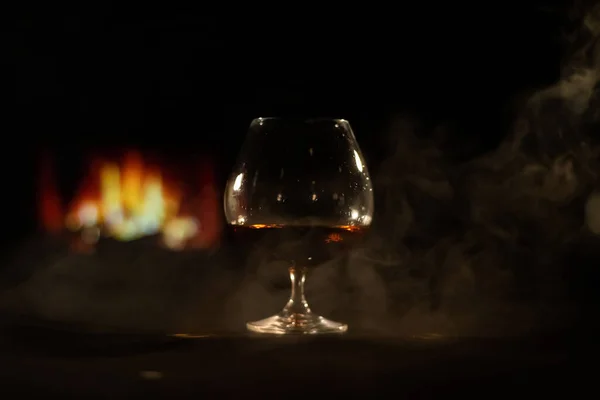 A glass of brandy and cigar smoke in the dark on the background of the fireplace. Gentlemens club concept