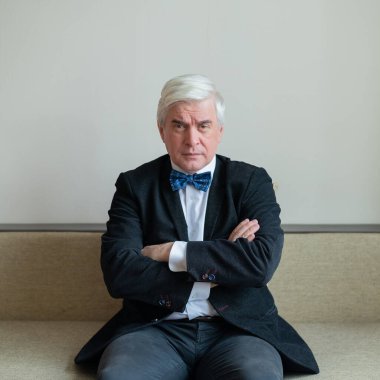 Memnun olmayan takım elbiseli ve papyonlu bir iş adamı kollarını göğsünde kavuşturarak oturur..