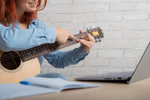 Eine Frau bringt sich online das Gitarrespielen bei. Musikunterricht aus der Ferne auf dem Laptop — Stockfoto