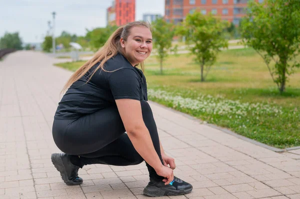 Eine dicke Frau im Trainingsanzug kauert und bindet ihre Schnürsenkel im Freien. — Stockfoto