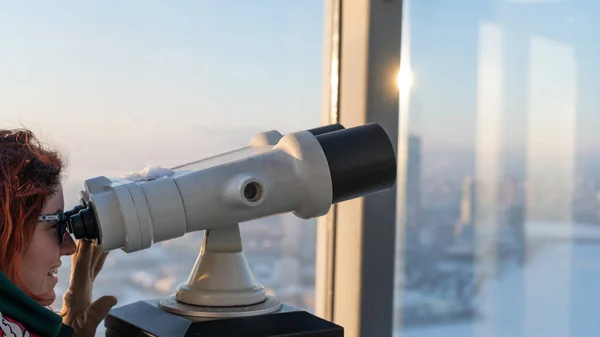 Una mujer mira a través de los prismáticos en la plataforma de observación de un rascacielos —  Fotos de Stock