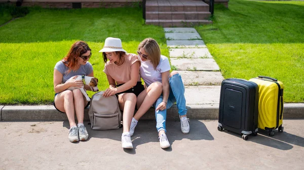 Drei kaukasische Frauen und ein Hund gehen auf Roadtrip. Die Mädchen laden ihre Koffer in den Kofferraum des Autos. Sommerferienkonzept mit Freundinnen. — Stockfoto