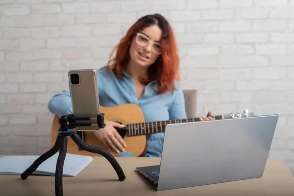 Egy nő online sugároz otthon a telefonján. A lány élőben énekel és gitározik. — Stock Fotó