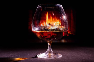 Şöminenin arka planında, karanlıkta bir bardak brendiye yakından bak.