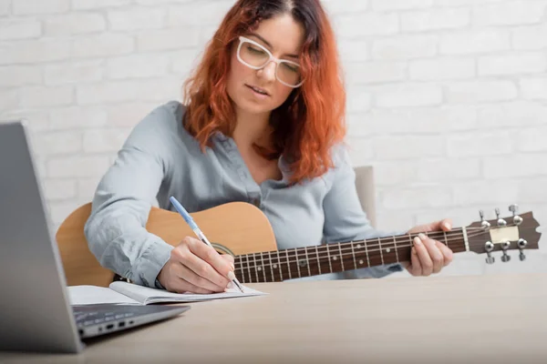 Een vrouw met een gitaar schrijft notities in een notitieboekje. Het meisje componeert een lied — Stockfoto