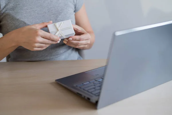 Online sale of gifts. A woman is holding a gift box in front of a laptop