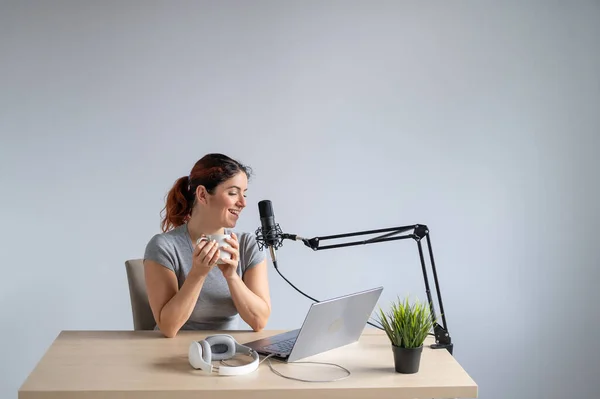 Une femme diffuse en ligne sur un ordinateur portable et boit du café. Animatrice radio sur le lieu de travail — Photo