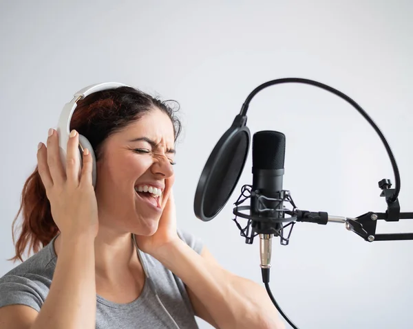 Egy nő fejhallgatóval felvesz egy dalt egy stúdióban. Az érzelmes lány örömmel énekel. — Stock Fotó