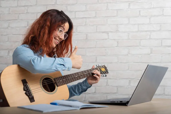 Кавказька жінка віддалено викладає гру на гітарі на ноутбуку. Тренування музики в Інтернеті — стокове фото