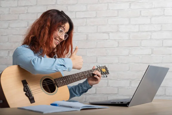 Kaukasierin unterrichtet aus der Ferne am Laptop das Gitarrespielen. Online-Musikschulung — Stockfoto