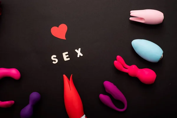 L'inscription coeur de sexe et une collection de vibromasseurs multicolores sur un fond noir. Jouets sexuels de différentes formes. Assortiment de sex shop — Photo