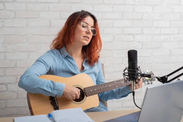 Eine Frau singt in ein Mikrofon und spielt die Gitarre live auf einem Laptop. Musikerin nimmt Videoblog auf — Stockfoto