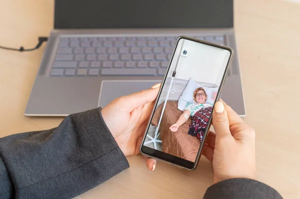 Mujer de negocios hace una videollamada en un teléfono inteligente a una madre anciana enferma en un hospital — Foto de Stock