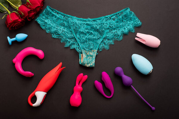 Top view of womens lace green panties red roses and different sex toys. Collection of multi-colored vibrators and underwear