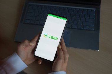 18 Ekim 2020 Rusya, Novosibirsk: Ekranda yeni Sberbank logosu olan bir kadın akıllı telefon tutuyor