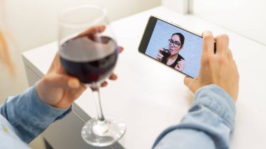 Kadınlar telefonda video iletişimi üzerinden konuşuyor ve kırmızı şarap içiyorlar. Karantina altındaki kız video araması yapmıyor.