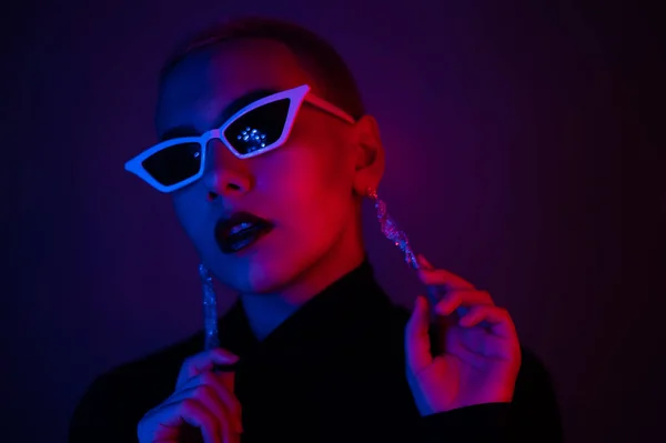 Porträtt av en ung kvinna med en kort manlig frisyr i solglasögon i neonljus i studion — Stockfoto