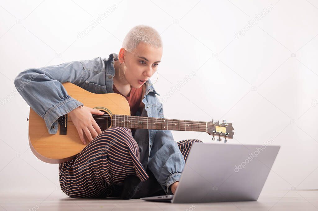 Young hipster woman watching guitar tutorials on laptop. Distance learning music