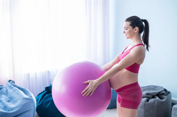 Una mujer embarazada en ropa deportiva está haciendo gimnasia para mujeres embarazadas. La muchacha se ocupa de la aptitud con la pelota para las mamás embarazadas. Último trimestre. —  Fotos de Stock