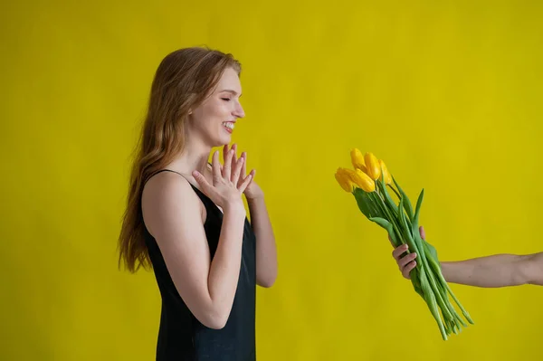 Mulher branca aceita tulipas como um presente no fundo amarelo. — Fotografia de Stock