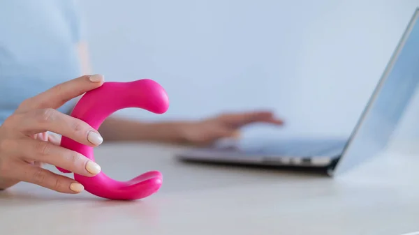 A woman sits at a laptop and holds a curved vibrator in her hands. The girl has online sex. — Stock Photo, Image