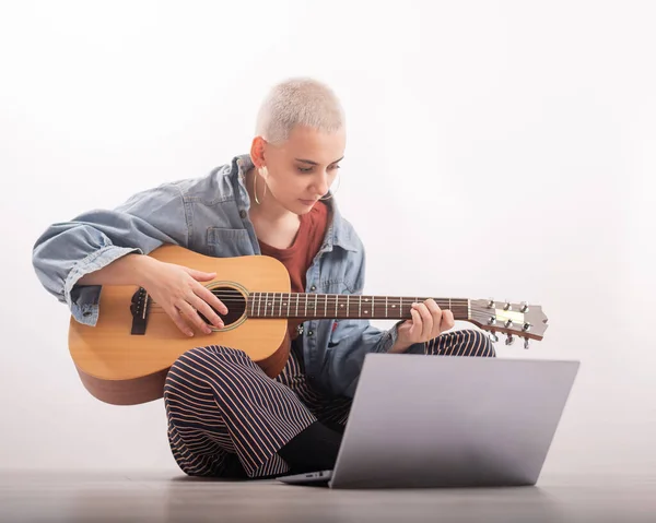 Jonge hipster vrouw die gitaarles kijkt op laptop. Muziek voor afstandsonderwijs — Stockfoto