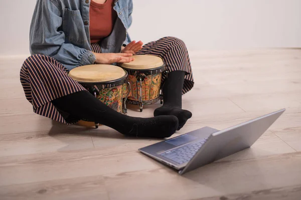 En ansiktslös kvinna sitter på golvet hemma och tittar på utbildningsvideor av att spela mini bongs. Flicka lär sig spela traditionella etniska trummor på distans. — Stockfoto