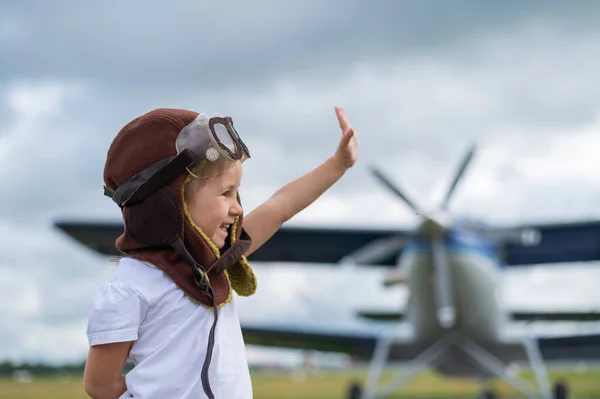 Una linda niña vestida con una gorra y gafas de un piloto en el fondo de un avión. El niño sueña con convertirse en piloto. —  Fotos de Stock
