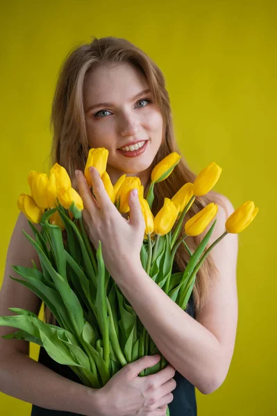 白种人女人，黄色背景上抱着一抱黄色郁金香。国际妇女日。春花花束 — 图库照片