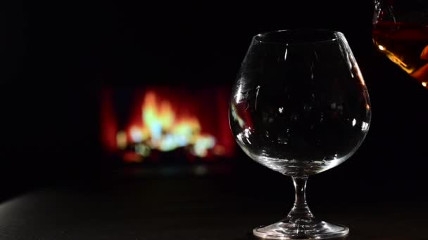 Häll brandy i ett glas mot bakgrund av den öppna spisen — Stockvideo