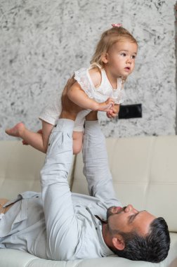 Beyaz bir adam kanepede uzanıyor ve küçük bir kızı üzerinde tutuyor. Şefkatli bir baba çocuğu büyüttü. Mutlu babalar.