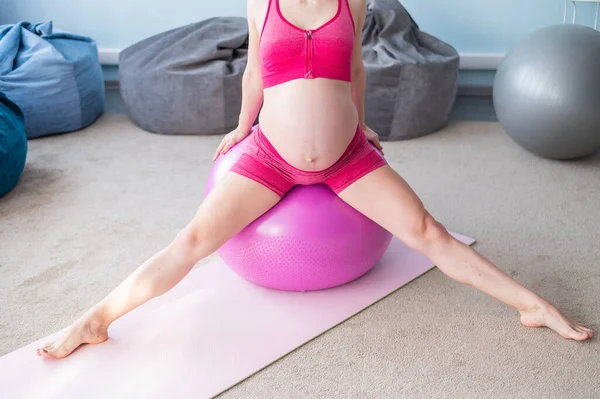 在瑜伽课上看到一个无法辨认的孕妇.未来的母亲，赤裸的肚子，正与一个球一起健身. — 图库照片