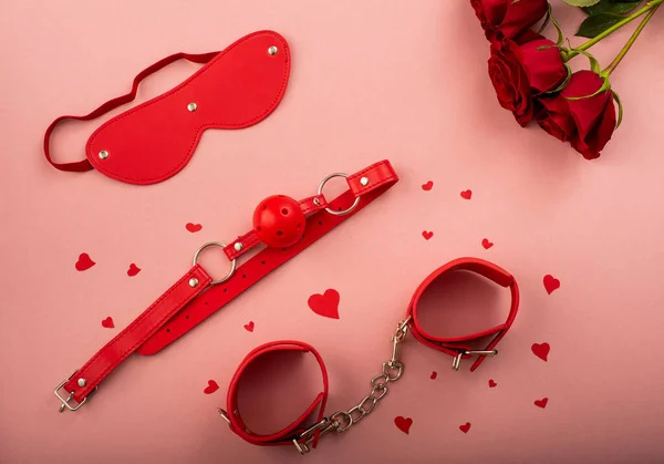 BDSM sada červené barvy a kytice růží na růžovém pozadí. Symbol lásky pro Valentýna. — Stock fotografie