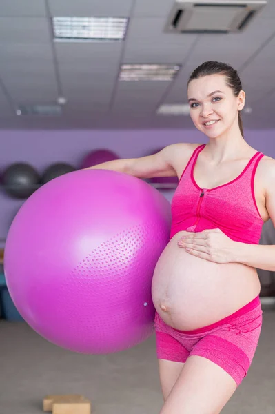 Una donna incinta in abbigliamento sportivo sta facendo ginnastica per le donne incinte. La ragazza è impegnata in idoneità con una palla per madri incinte. Ultimo trimestre. — Foto Stock