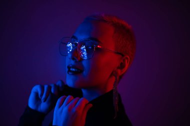 Kısa saçlı, neon ışıklı gözlük takan genç sarışın kadının yakın plan portresi.