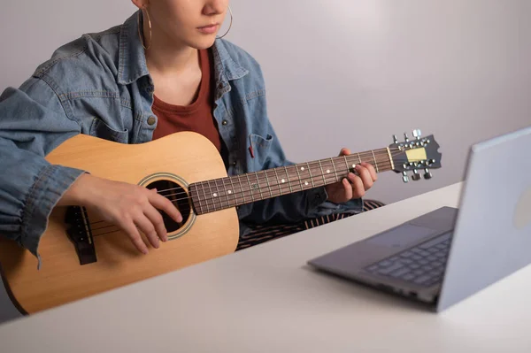 Jonge vrouw leert online gitaar spelen. Remote muzieklessen op een laptop — Stockfoto