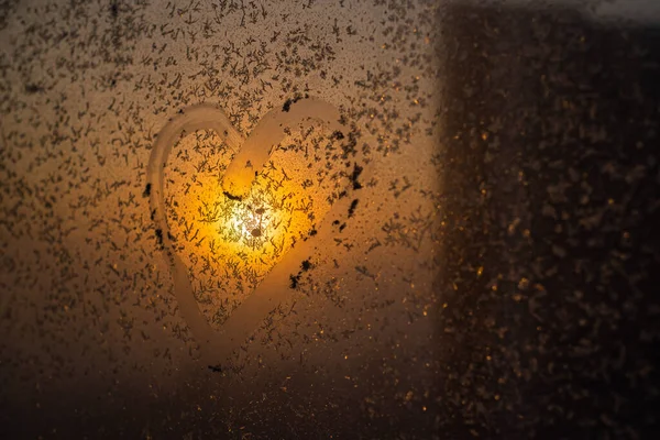 Un cuore disegnato su una finestra invernale ghiacciata al tramonto. — Foto Stock