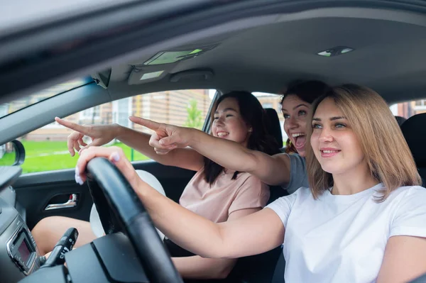 Três amigos vão numa viagem. Mulheres caucasianas dirigem em um carro e apontam os dedos de surpresa. — Fotografia de Stock