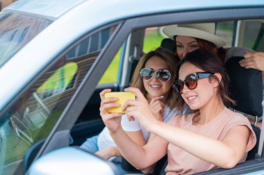 Üç mutlu kız arkadaş bir yolculuğa çıkıyor. Kadınlar arabaya binip cep telefonuyla selfie çekiyorlar.