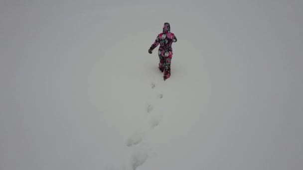 Une fille en salopette colorée marche dans la neige. Vue arrière depuis le drone — Video