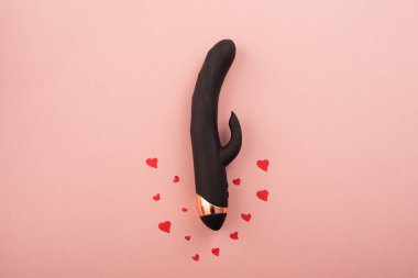 Black clitoral vaginal dildo and hearts on a pink background. Female vibrator as a gift for Valentines Day. Copy space