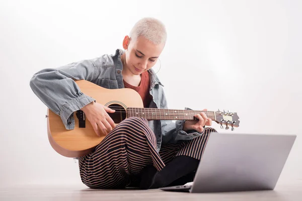 Jonge hipster vrouw die gitaarles kijkt op laptop. Muziek voor afstandsonderwijs — Stockfoto