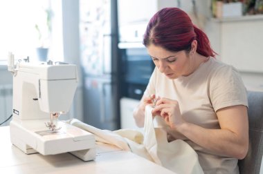 Beyaz kadın mutfakta otururken dikiş dikiyor. Ev hobisi