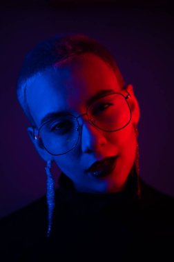 Kısa saçlı, neon ışıklı gözlük takan genç sarışın kadının yakın plan portresi.