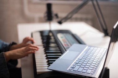 Elektrikli piyanonun kadın ellerine yakın çekim. Bir kadın dizüstü bilgisayarda sentezleyici çalmayı öğreniyor.