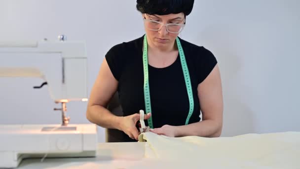 Professionell sömmerska skär material med sax på en vit bakgrund. Kvinna som arbetar på en symaskin. — Stockvideo