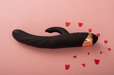 Black clitoral vaginal dildo and hearts on a pink background. Female vibrator as a gift for Valentines Day